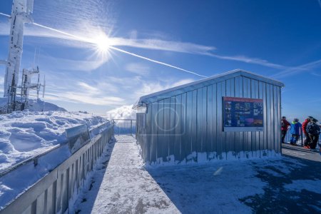 Téléchargez les photos : Une vue captivante depuis le paysage enneigé de San Pellegrinos sous un ciel bleu clair, avec des skieurs près d'une planche d'information et des sommets montagneux escarpés baignés de soleil au loin. - en image libre de droit