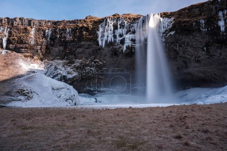 landscape of a huge snowy and icy waterfall with blue sky and autumn scenery