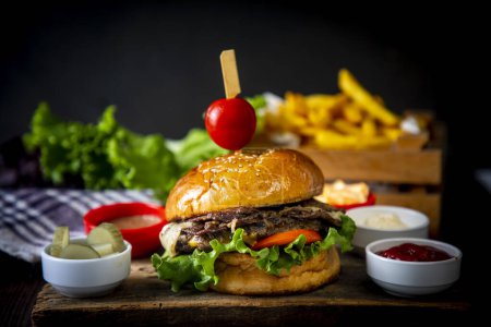 Téléchargez les photos : Hamburger maison servi avec des frites. Il a l'air délicieux préparé avec des oignons, galettes de hamburger, fromage cheddar et jambon. - en image libre de droit