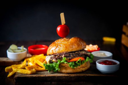 Photo for Homemade hamburger served with french fries. It looks delicious prepared with onions, hamburger patties, cheddar cheese and ham. - Royalty Free Image