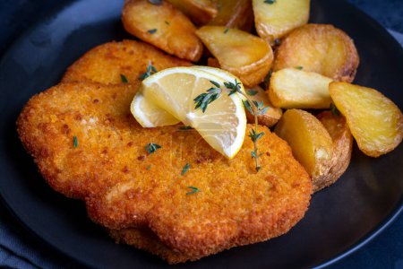 Téléchargez les photos : Chicken schnitzel with sauce, fried potatoes and lemon in a plate - en image libre de droit