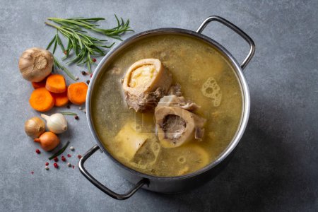 Photo for Boiled bone and broth. Homemade beef bone broth is cooked in a pot on. Bones contain collagen, which provides the body with amino acids, which are the building blocks of proteins. - Royalty Free Image