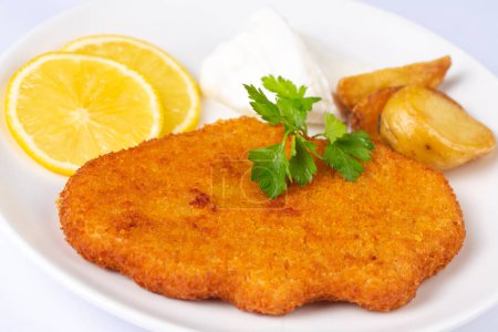 Téléchargez les photos : Chicken schnitzel with sauce, fried potatoes and lemon in a plate - en image libre de droit