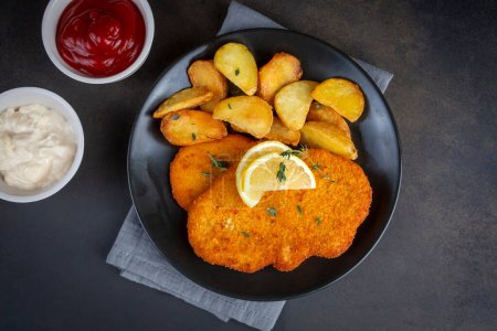 Foto de Chicken schnitzel with sauce, fried potatoes and lemon in a plate - Imagen libre de derechos