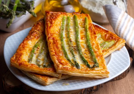 Photo for Baked green asparagus with ham and cheese in puff pastry sprinkled with sesame seeds and green basil leaves. - Royalty Free Image