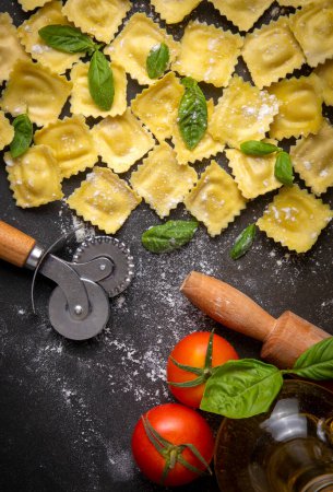 Foto de Delicious raw ravioli with flour and basil on dark background. The process of making Italian ravioli. - Imagen libre de derechos