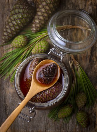 Photo for Young pine cones jam in glass bowl on wooden board. Delicious jam with the little pine cones. - Royalty Free Image