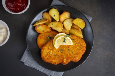 Foto de Chicken schnitzel with sauce, fried potatoes and lemon in a plate - Imagen libre de derechos