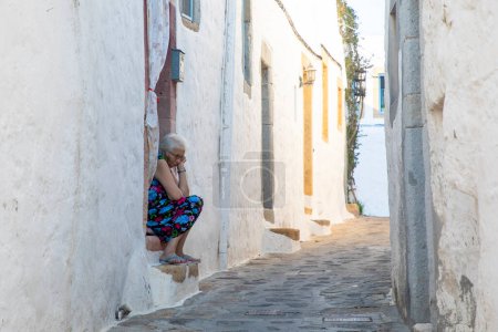 Téléchargez les photos : Île de Patmos - Grèce, 3 juillet 2022, Une vieille femme assise dans les rues de l'île de Patmos - en image libre de droit