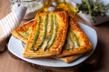 Photo for Baked green asparagus with ham and cheese in puff pastry sprinkled with sesame seeds and green basil leaves. - Royalty Free Image