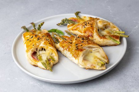 Photo for Baked green asparagus with ham and cheese in puff pastry sprinkled with sesame seeds - Royalty Free Image