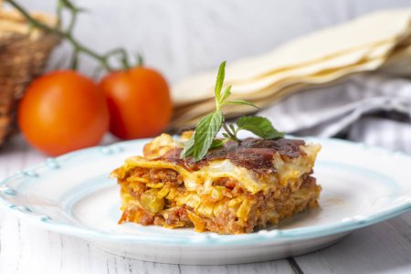 Foto de Portion of ground beef lasagna topped with melted cheese and garnished with fresh parsley served on a plate in close view for a menu - Imagen libre de derechos