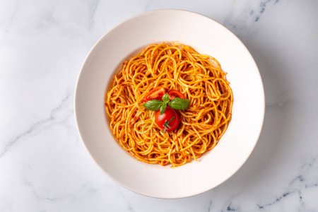 Foto de Sabroso y apetitoso clásico pasta de espagueti italiano con salsa de tomate, queso parmesano y albahaca en el plato e ingredientes para cocinar pasta en la mesa de mármol blanco. - Imagen libre de derechos