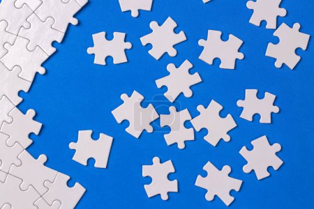Téléchargez les photos : Missing jigsaw puzzle pieces. Business concept. Fragment of a folded white jigsaw puzzle and a pile of uncombed puzzle elements against - en image libre de droit