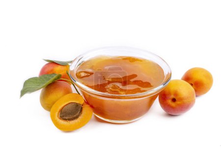 Téléchargez les photos : Bol en verre avec confiture d'abricot sucrée et fruits frais sur fond blanc - en image libre de droit