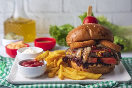 Foto de Homemade hamburger served with french fries. It looks delicious prepared with onions, hamburger patties, cheddar cheese and ham. - Imagen libre de derechos