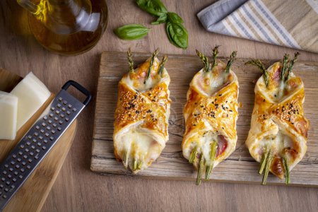 Téléchargez les photos : Baked green asparagus with ham and cheese in puff pastry sprinkled with sesame seeds and green basil leaves. - en image libre de droit