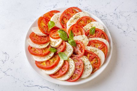 Foto de Ensalada caprese italiana con tomates en rodajas, mozzarella, albahaca, aceite de oliva - Imagen libre de derechos