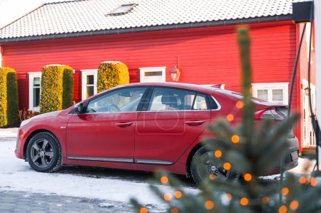 Foto de Tnsberg, Noruega - 2 de diciembre de 2023: coche eléctrico Hyundai Ioniq rojo anaranjado que se carga junto a la casa noruega - Imagen libre de derechos