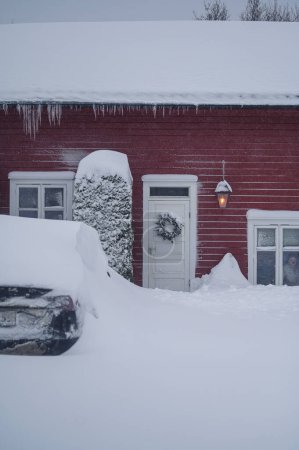 Foto de Tonsberg, Noruega - 1 de enero de 2024: Coche eléctrico Hyundai Ioniq rojo anaranjado bajo la nieve. Una tormenta de nieve. Eliminación de nieve por soplador de nieve - Imagen libre de derechos