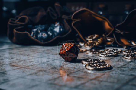 A red role-playing gaming die on a gaming grid with game coins and dice bags