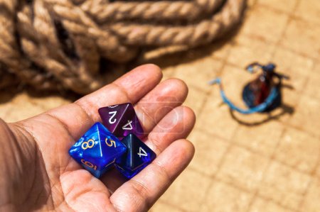 Photo for Hand holding three d8 dice, two blue, one purple, with RPG battlemap and figurine in the backdrop. Used for DnD and other role-playing games - Royalty Free Image