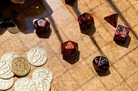 Photo for Overhead shot featuring a collection of vibrant red RPG dice and golden gaming coins arranged on a battle map - Royalty Free Image