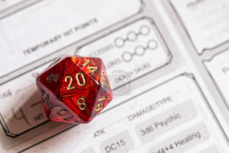 Photo for Sharp focus on a red D20 die resting on a detailed role-playing game character sheet, symbolizing strategy and chance in gaming - Royalty Free Image