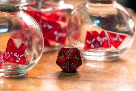A single red die stands prominently in focus, contrasting with blurred dice in glass jars in the background, on a rustic wooden table