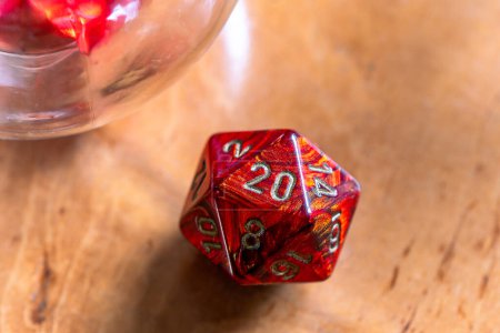 Close-up of a vibrant red D20 die, emphasizing its detailed markings on a warm wooden background, perfect for gaming and fantasy themes.