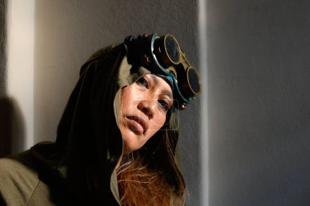 n engaging portrait of a hooded woman wearing steampunk goggles, her face lit by a bold stream of sunlight, creating a dynamic interplay of light and shadow