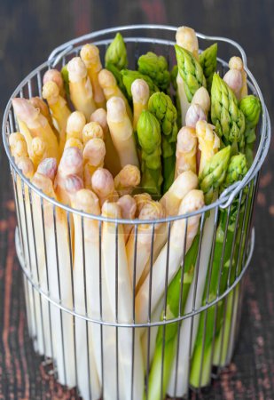 Foto de New harvest of German white and green asparagus, bunch of raw green and white asparagus in basket with background of wood - Imagen libre de derechos