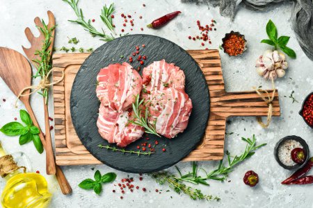 Photo for Raw cutlets in bacon served on a black plate with rosemary and thyme. On a gray background. Top view. - Royalty Free Image
