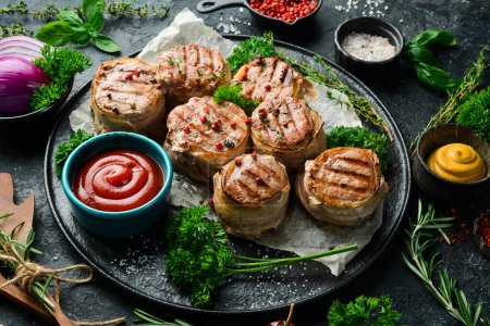 Photo for Grilled medallions wrapped in bacon. in a pan, ready to eat. On a black concrete background. Top view. - Royalty Free Image