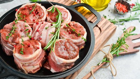 Téléchargez les photos : Médaillons de viande crue enveloppés dans du bacon. dans une casserole, prête à cuire. Sur un fond concret. Vue latérale. - en image libre de droit