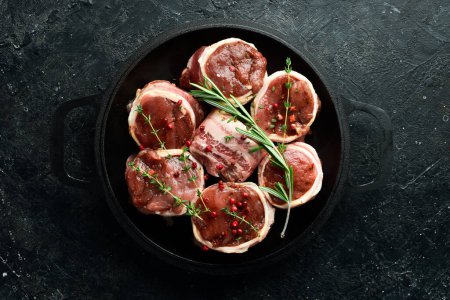 Photo for Meat. Raw Meat Veal medallions wrapped in bacon. Laid out in a pan, ready to cook. On a black concrete background. Top view. - Royalty Free Image