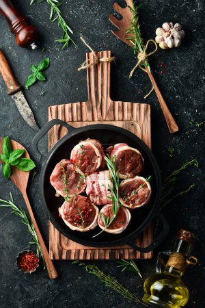 Photo for Meat. Raw Meat Veal medallions wrapped in bacon. Laid out in a pan, ready to cook. On a black concrete background. Top view. - Royalty Free Image