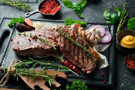 Photo for Juicy striploin steak grilled with spices and rosemary. On a black concrete background. Side view. - Royalty Free Image