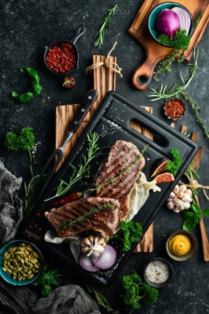 Photo for Barbecue. Grilled striploin steak with spices and rosemary. On a black concrete background. Free space for text. - Royalty Free Image