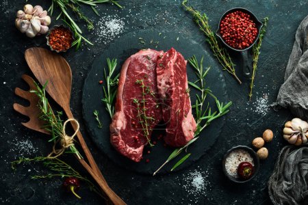 Photo for Raw juicy striploin steak. Fermented steak with rosemary and spices is ready for cooking. Meat. On a black stone background. Top view. - Royalty Free Image
