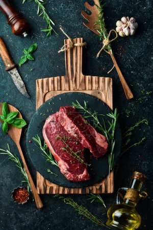 Photo for Raw juicy striploin steak. Fermented steak with rosemary and spices is ready for cooking. Meat. On a black stone background. Top view. - Royalty Free Image