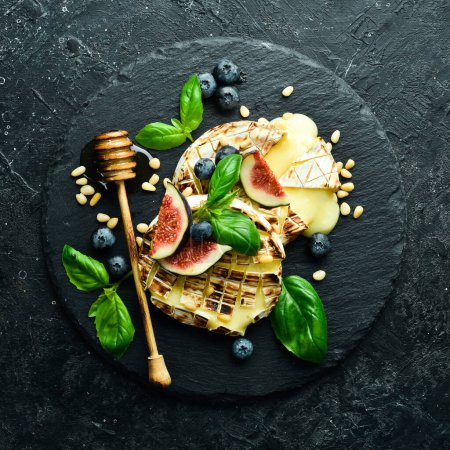 Photo for Baked brie cheese with figs, honey and blueberries. On a plate. On a black stone background. - Royalty Free Image