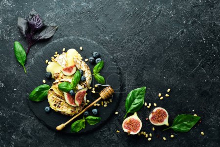 Photo for Baked brie cheese with figs, honey and blueberries. On a plate. On a black stone background. - Royalty Free Image