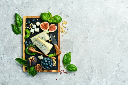 Photo for Sliced cheese on a board. Blue cheese, figs, blueberries and honey. On a concrete background. Top view. - Royalty Free Image
