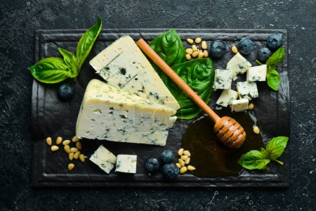 Photo for Blue cheese with mold on a black stone plate with basil and honey. On a black stone background. Top view. - Royalty Free Image