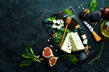 Téléchargez les photos : Fromage bleu avec moisissure sur une assiette en pierre noire avec basilic et miel. Sur un fond de pierre noire. Vue du dessus. - en image libre de droit