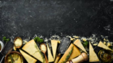 Téléchargez les photos : Contexte alimentaire déconcentré. Ensemble de fromages à pâte dure avec couteaux à fromage sur fond de pierre noire. Du parmesan. Vue de dessus. Espace libre pour votre texte. - en image libre de droit