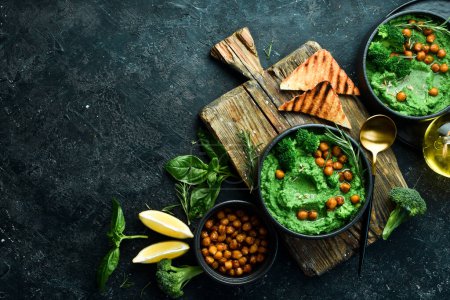 Photo for Green hummus. Hummus from chickpeas and spinach and broccoli, with olive oil and spices. Healthy vegetarian food. On a stone black background. - Royalty Free Image
