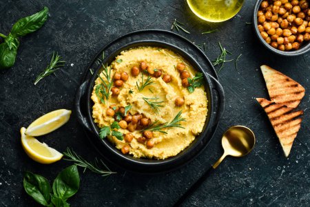Photo for Traditional vegetarian hummus with chickpeas in a bowl. Top view. On a black stone background. - Royalty Free Image