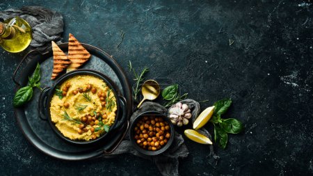 Photo for Hummus with chickpeas and rosemary in a black stone plate. Vegetarian food. Top view. On a black stone background. - Royalty Free Image